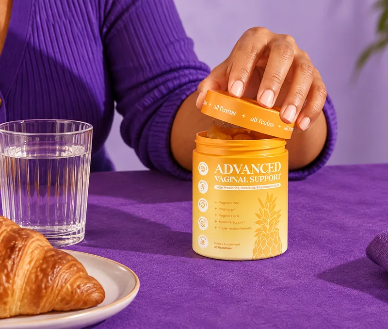 Woman taking a gummy from the jar of Advanced Vaginal Support at her kitchen table